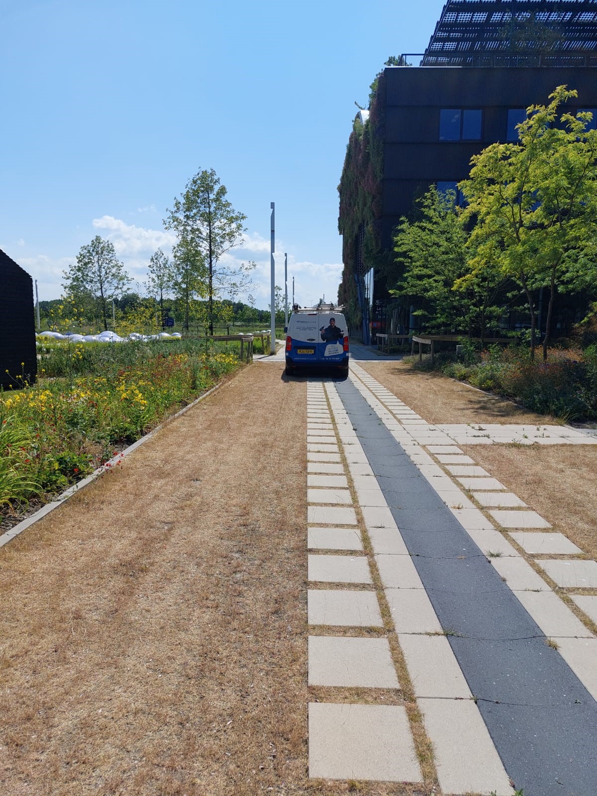 Servicebus van CameraInstallatie op het pad langs een gebouw met groene levende gevel en zonnepanelen op het terrein