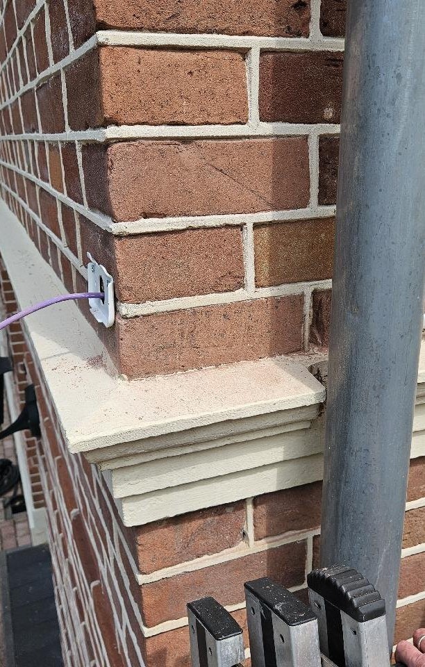 Netwerkkabel verdwijnt via een kleine doorvoer in het metselwerk vlak boven een geprofileerde raamdorpel