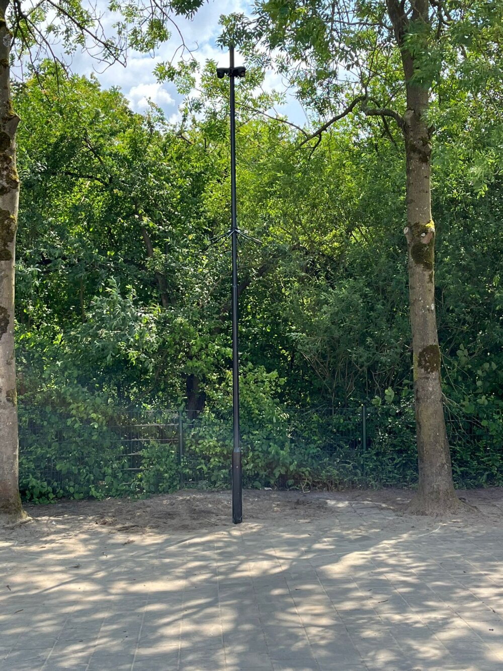 De zwarte camerapaal van zes meter op het bestrate schoolplein, met twee camera's op de kop
