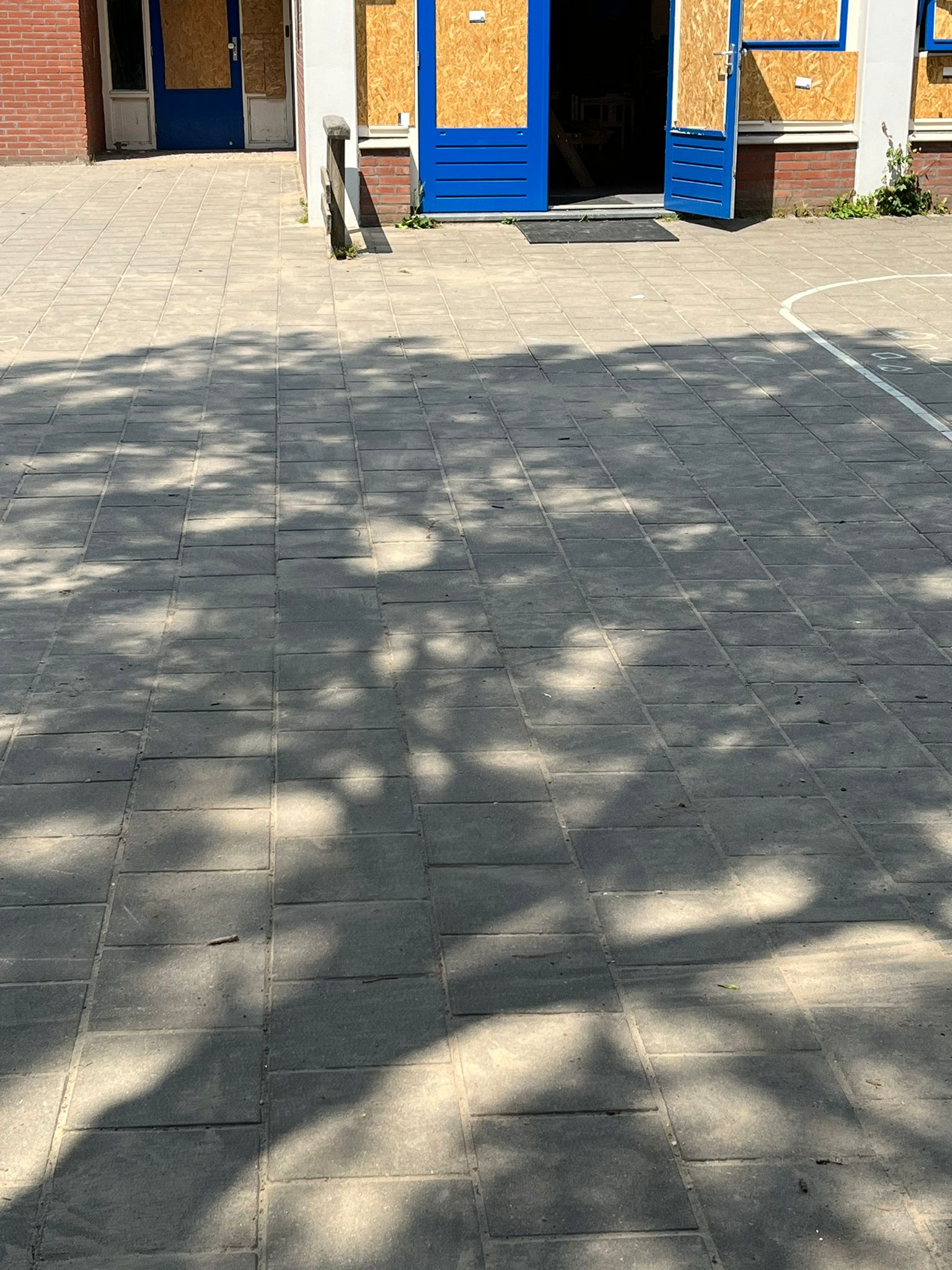Schoolplein met blauwe deuren en raamkozijnen die met houten platen zijn dichtgezet na de vernielingen