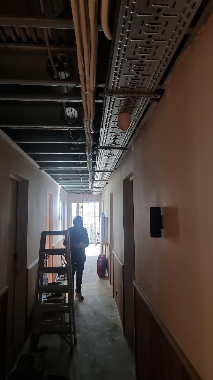 Hotelgang tijdens de bouw met dubbele rijen kabelgoten boven het plafond, een trapladder en een kabelhaspel op de vloer