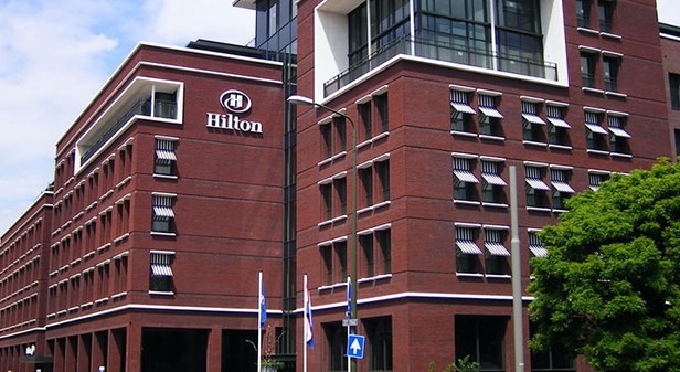 Bakstenen gevel van het Hilton Hotel in Den Haag met het hotellogo boven de zonneschermen