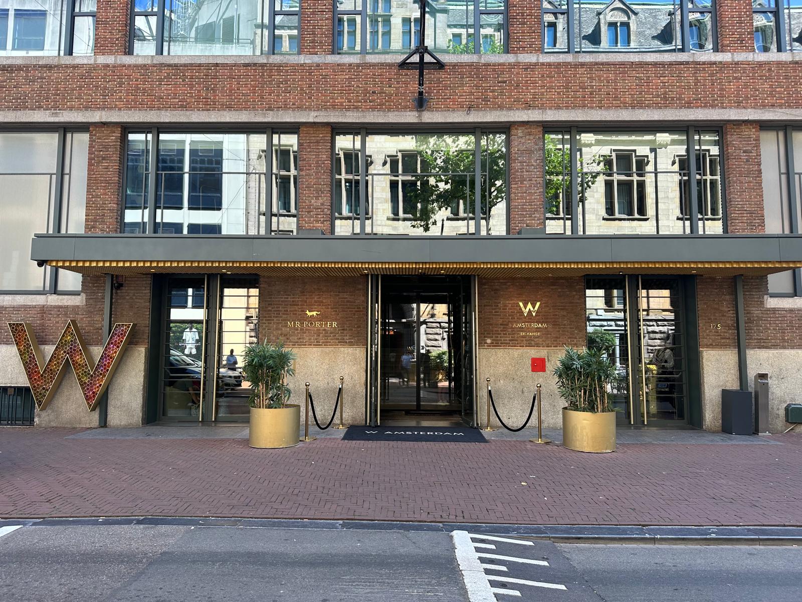 Bakstenen hotelgevel met gouden luifel boven de draaideur, met camera's onder de overkapping
