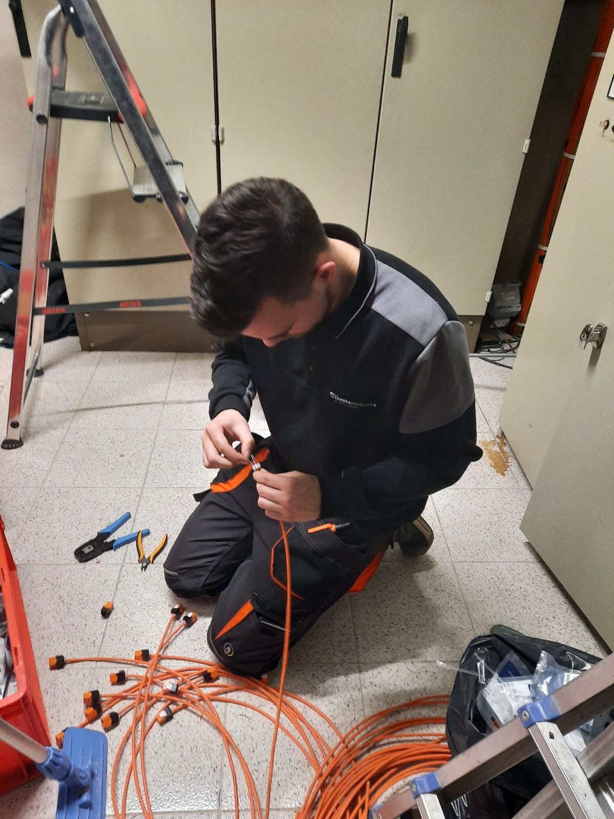 Monteur van CameraInstallatie monteert een oranje netwerkkabel af met een RJ45-stekker