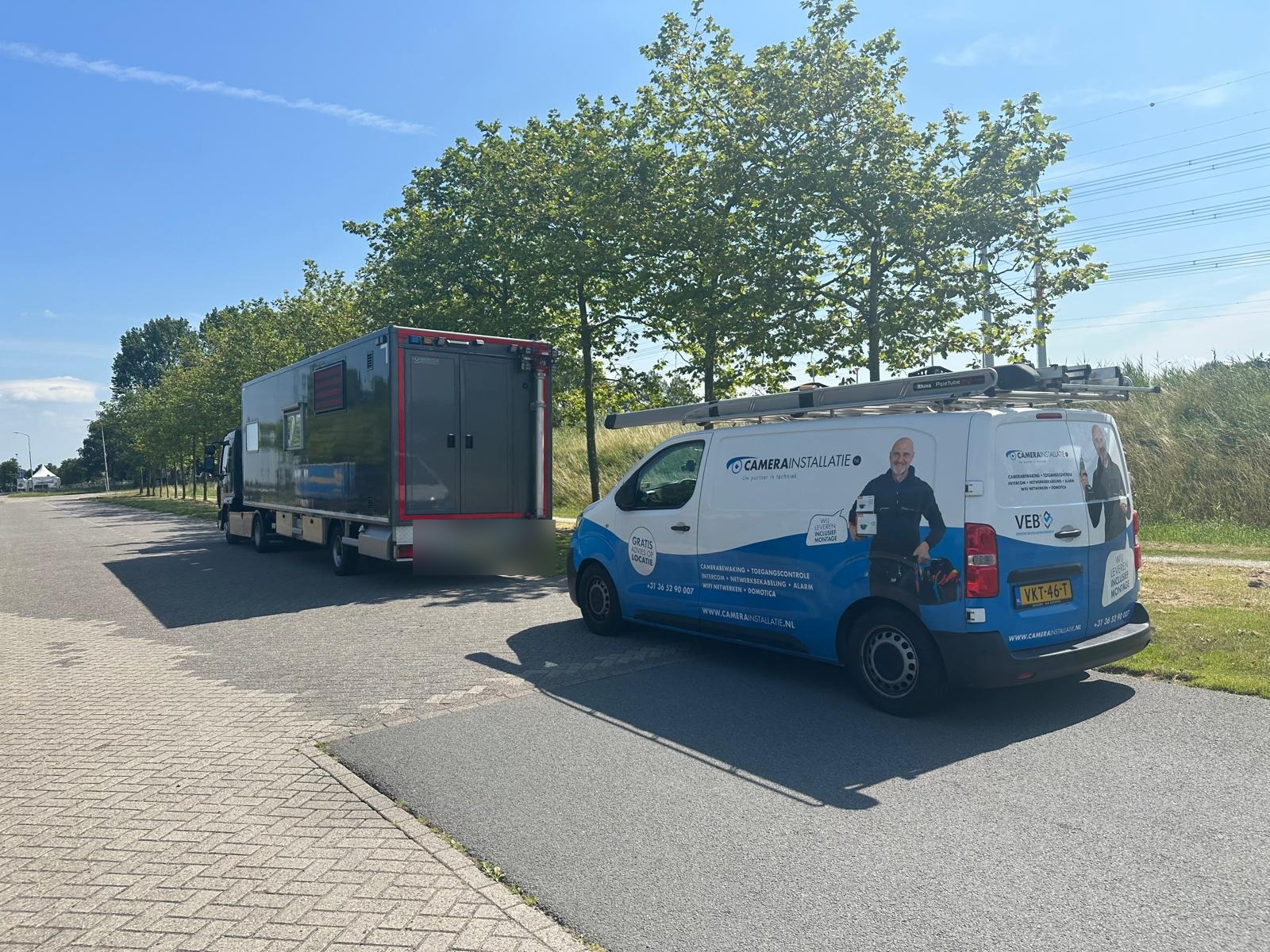 Vrachtwagen met een gesloten unit op de laadbak, geparkeerd naast de bestelbus van CameraInstallatie.nl langs een weg