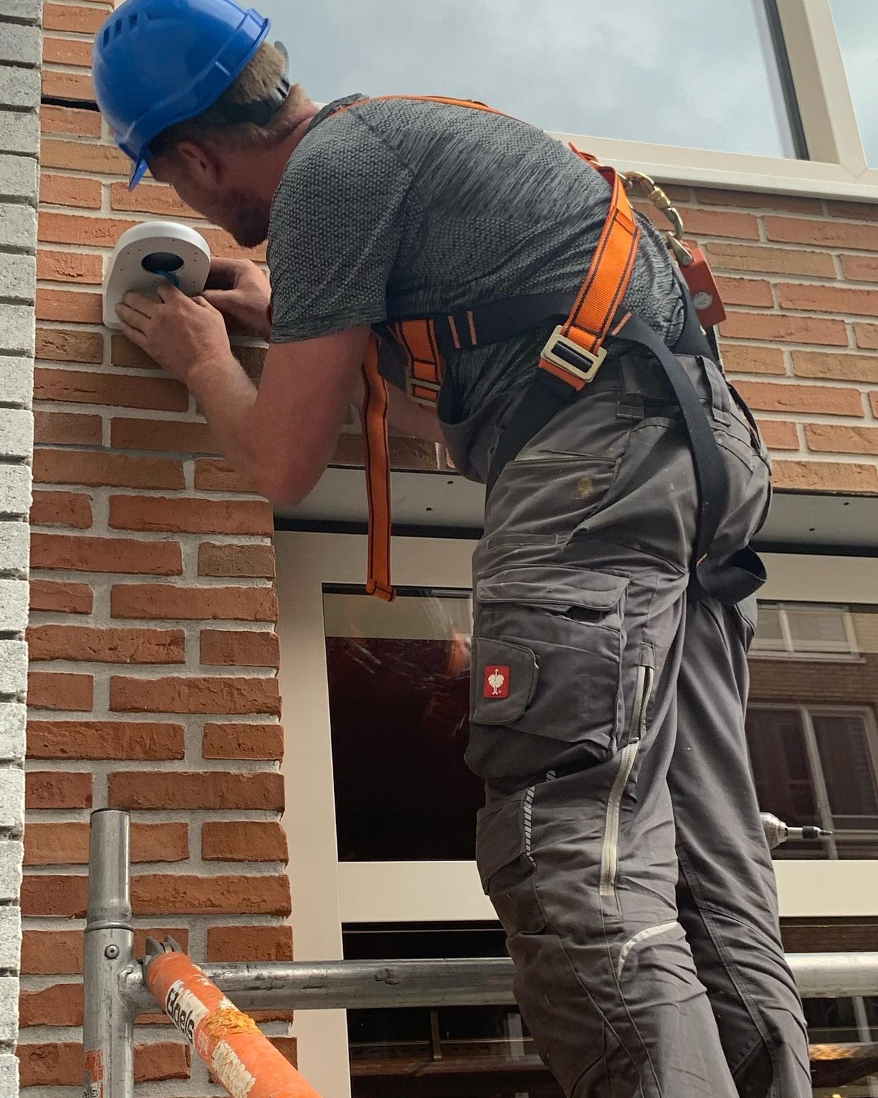 Monteur Marcel van CameraInstallatie monteert met harnas en helm een camera aan een bakstenen gevel