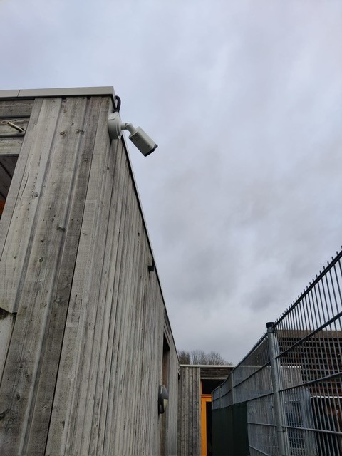 Zichtbare bullet-camera aan een bedrijfsgevel die het terrein overziet
