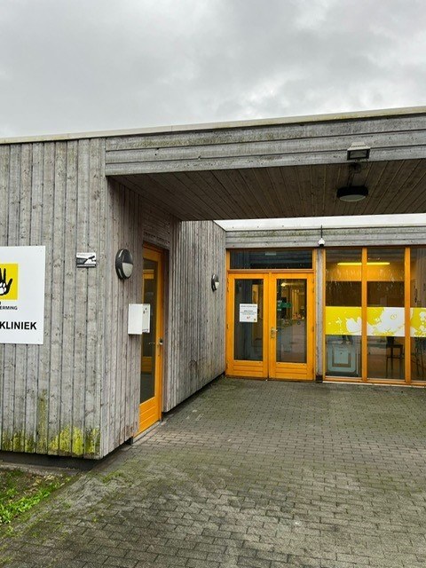 Ingang van de dierenkliniek met houten gevel, gele deuren en een camera onder de overkapping