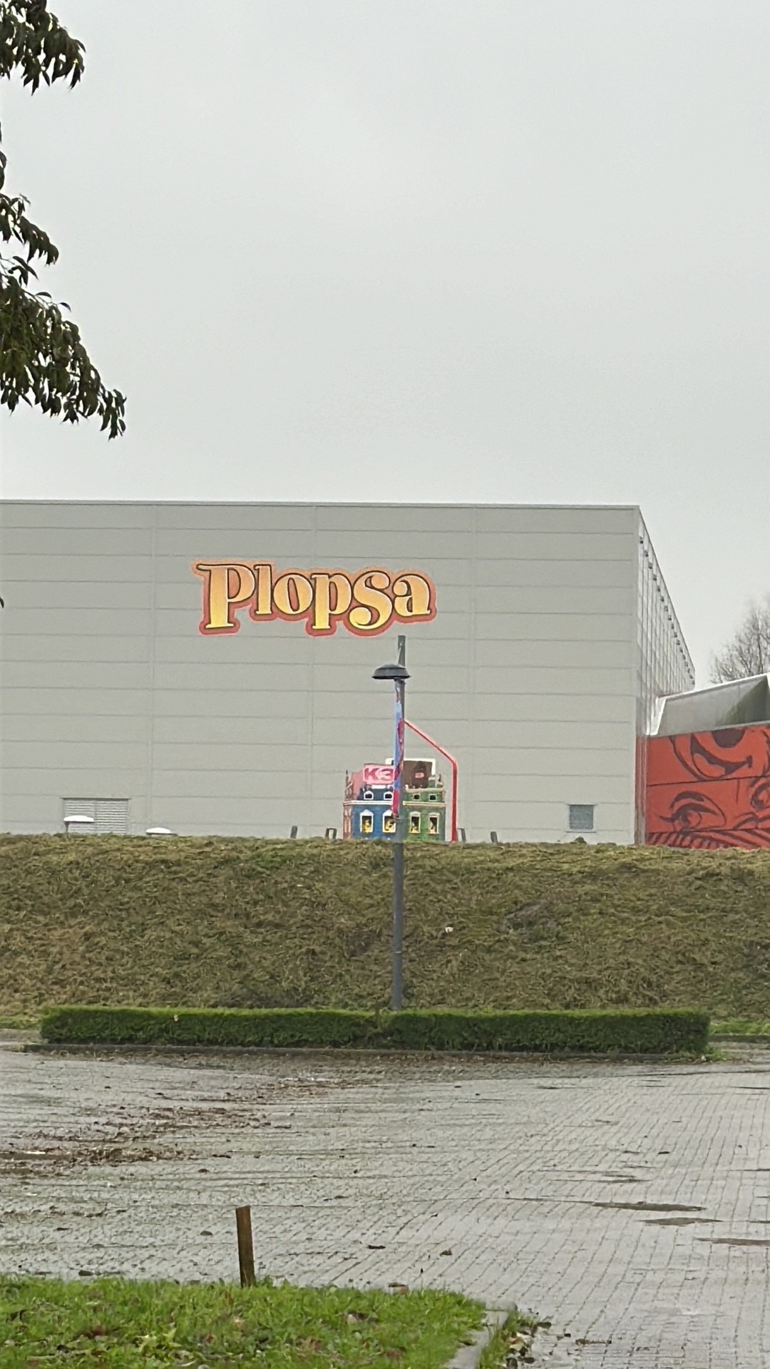Grijze hal van het indoor recreatiepark met de parknaam op de gevel, gezien vanaf de parkeerplaats