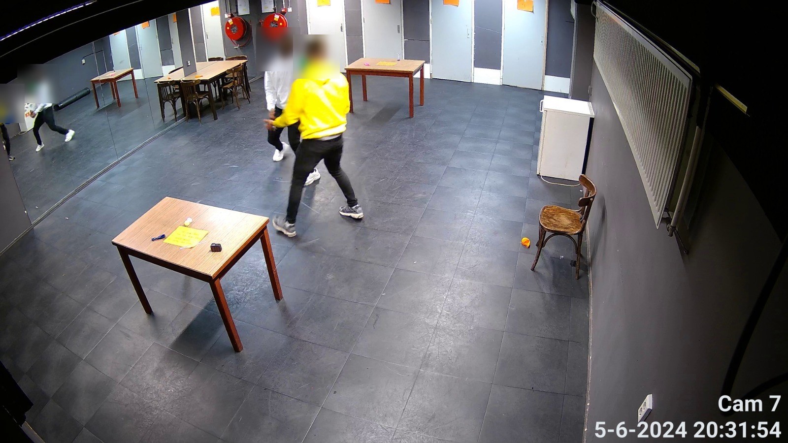 Camerabeeld van een ruimte met tafels en spiegelwand waarin twee personen bewegen
