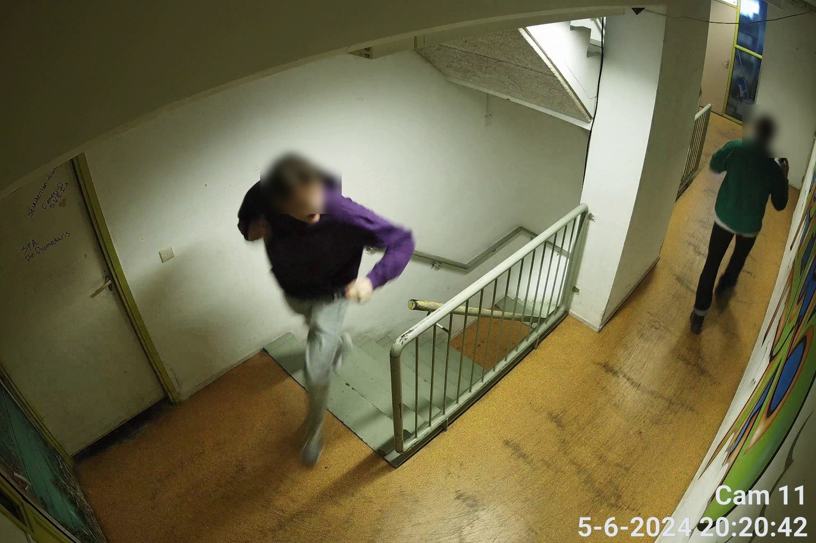 Camerabeeld van een trappenhuis met een persoon die de trap op komt en rechts een gang met een tweede persoon