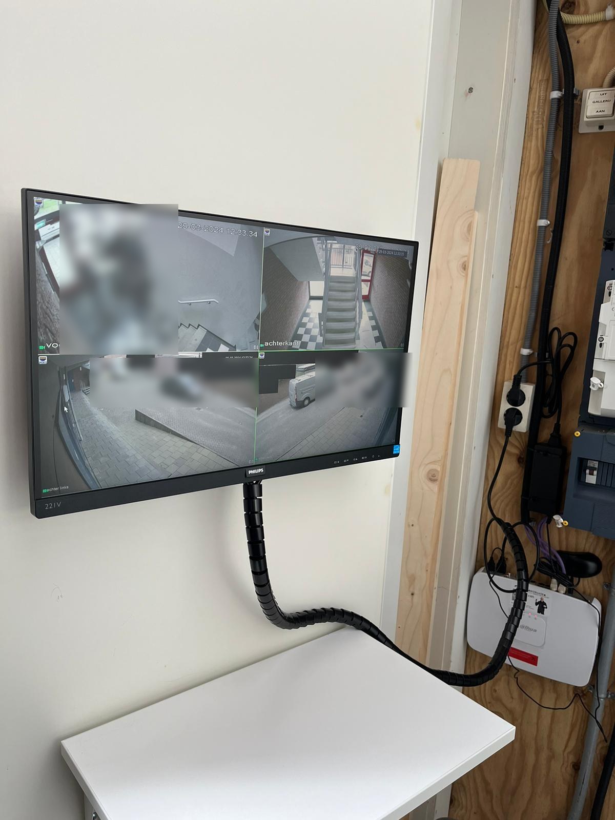Wandmonitor in een technische ruimte met vier camerabeelden naast elkaar, waarvan delen zwart zijn afgedekt
