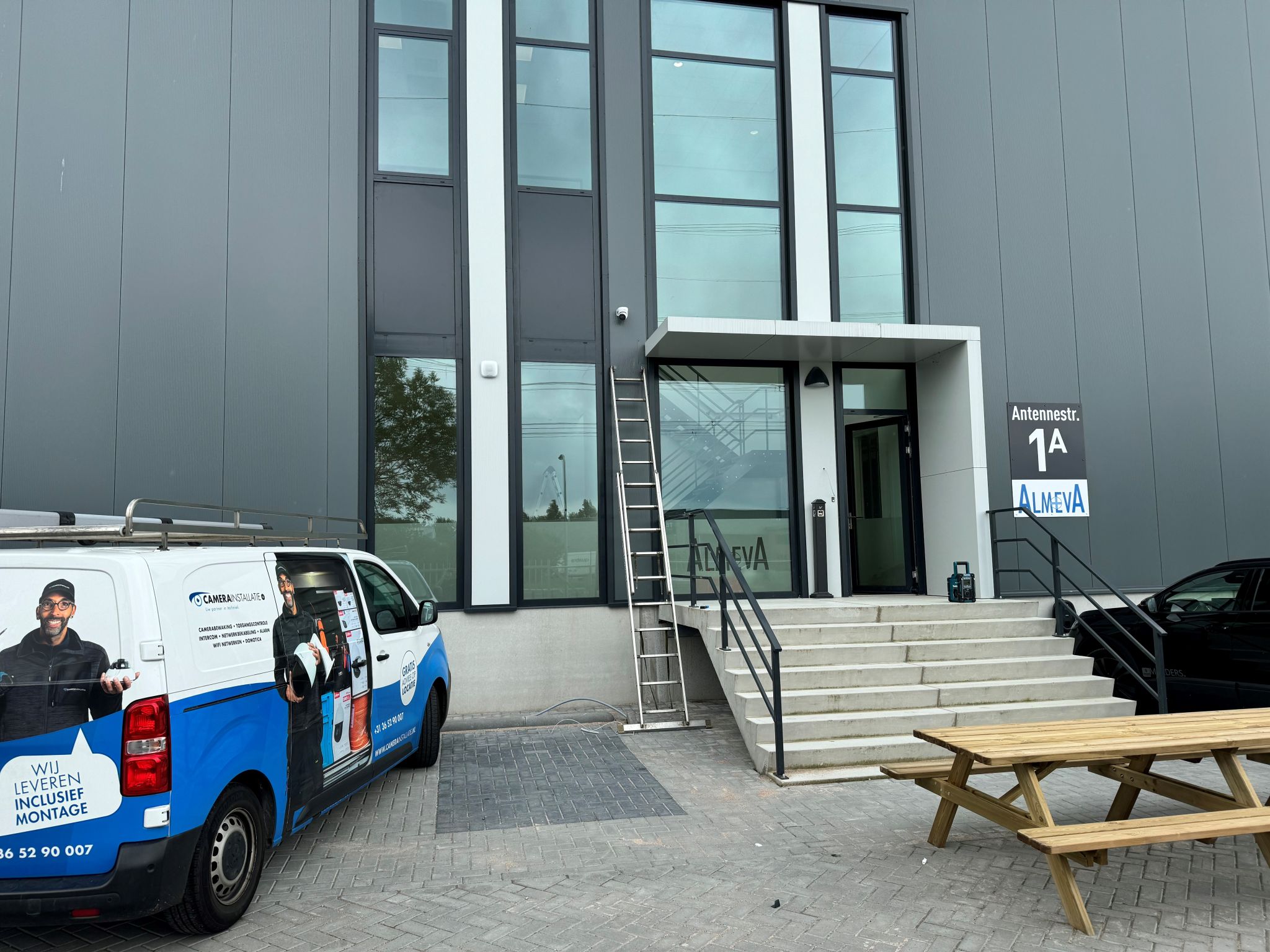 Bus van CameraInstallatie voor de entree van een gebouw, met een monteur die materiaal uitlaadt