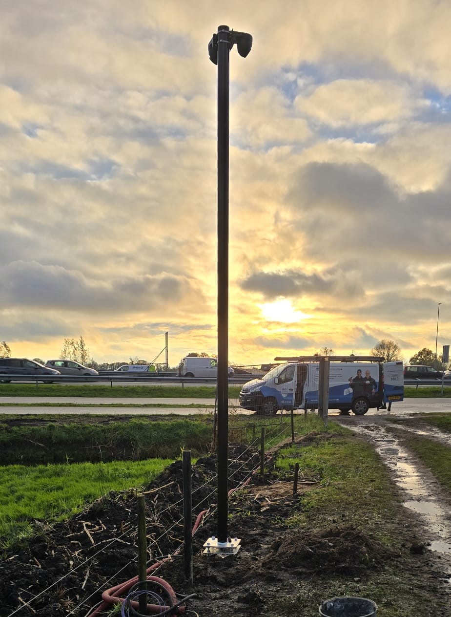 Cameramast bij zonsondergang langs de weg, met onze bedrijfsbus ernaast