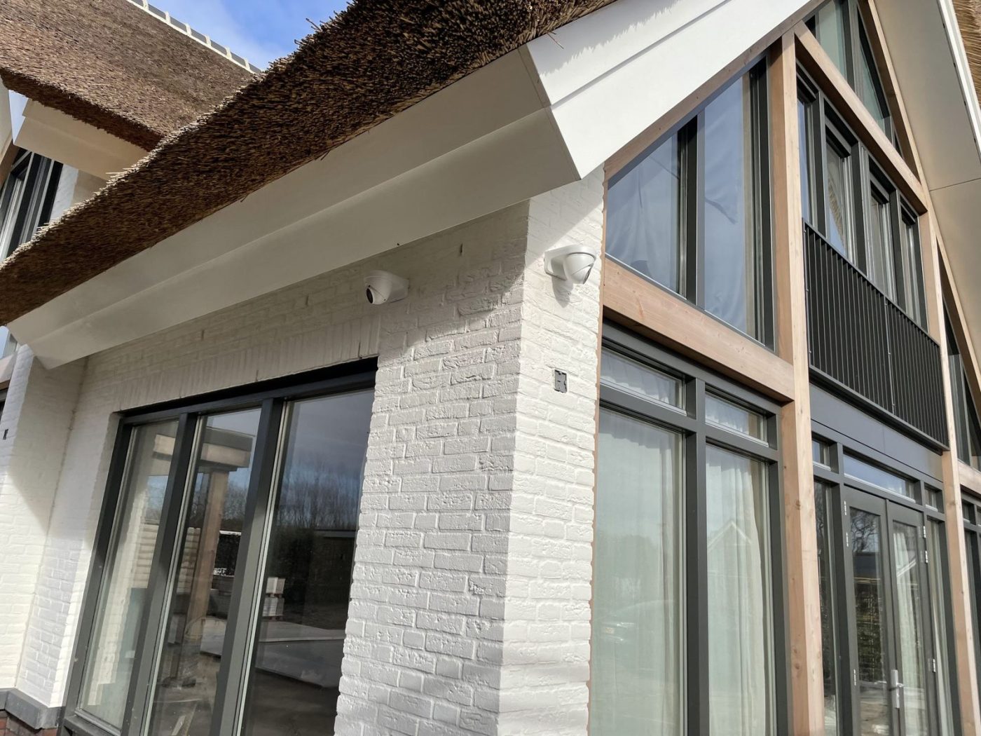 Witte camera onder de overstek en een camera op de hoek van een vrijstaande woning met rieten kap