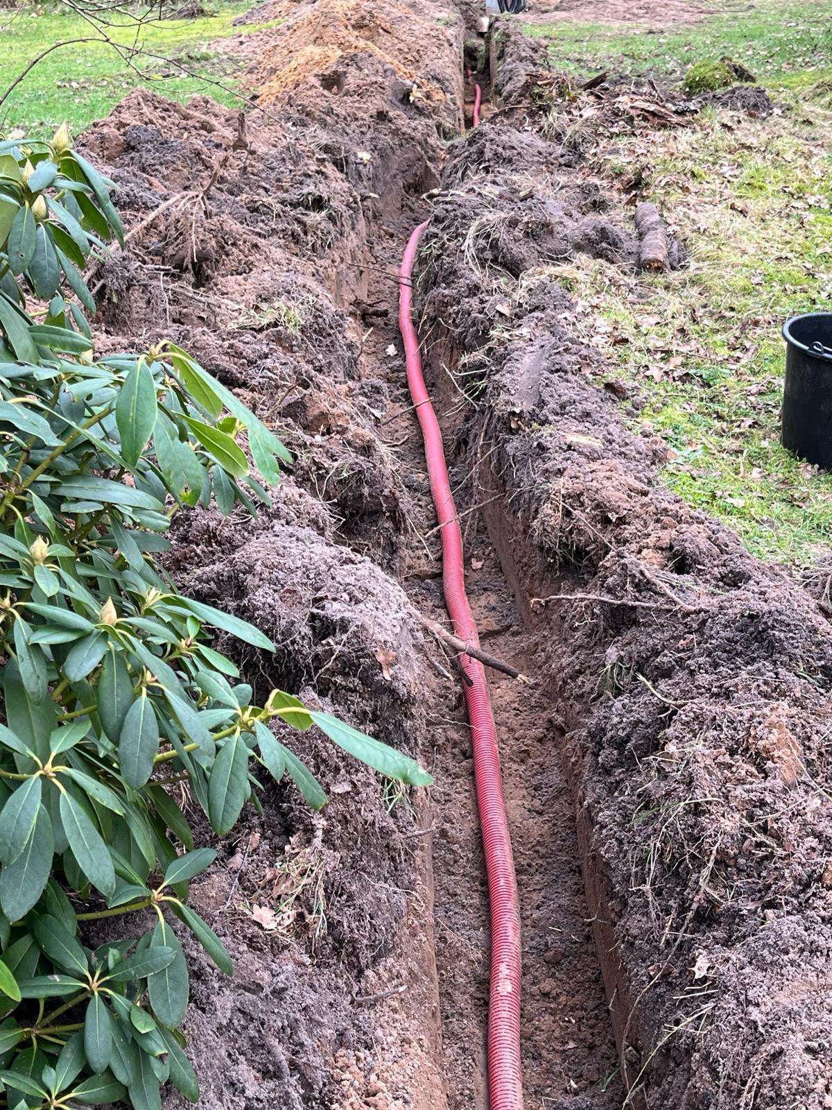 Open sleuf met een roze kabelbuis erin, dwars door een groenstrook