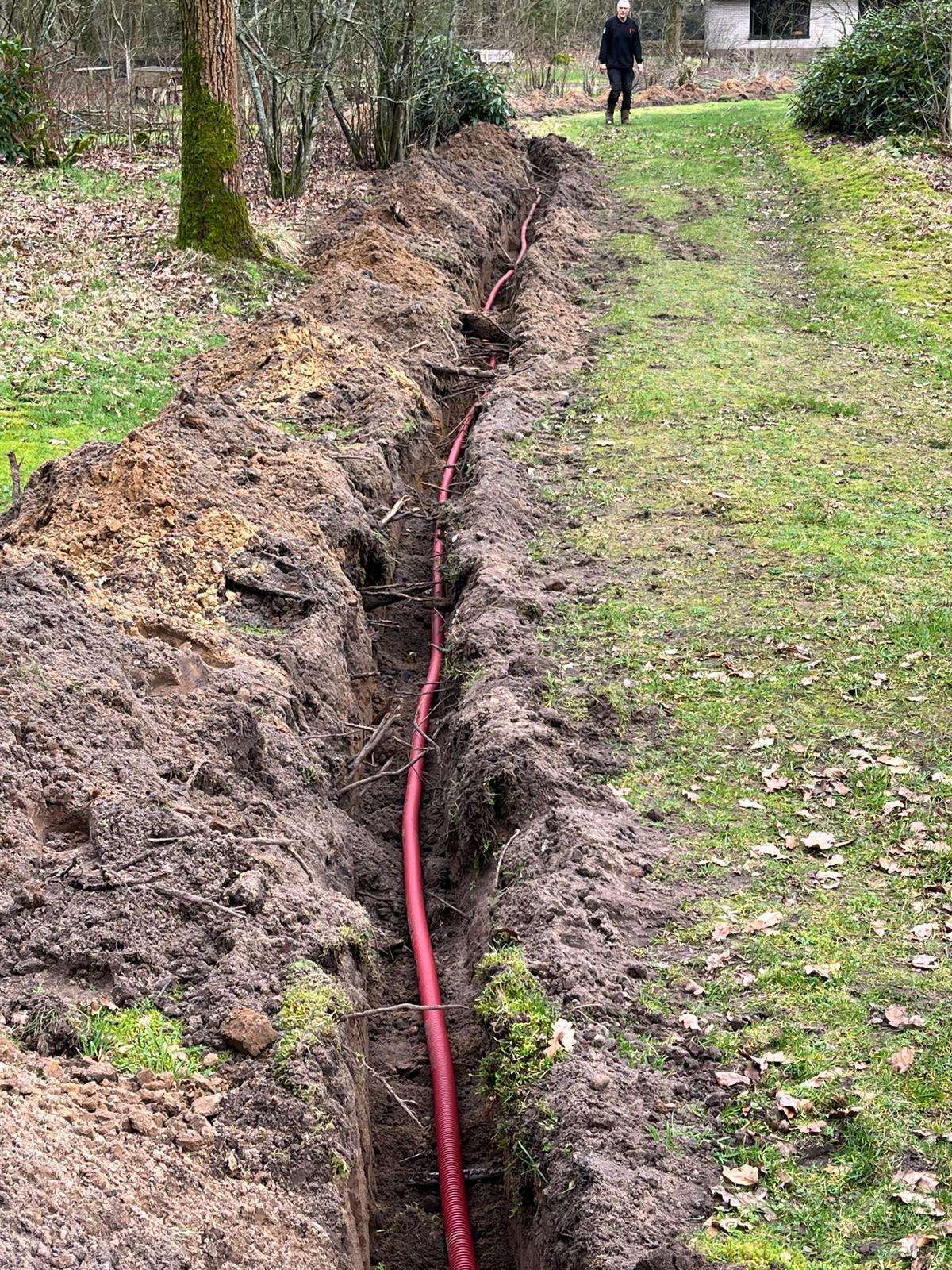 Sleuf door het gras met de rode kabelbuis erin, op weg naar een camerapaal