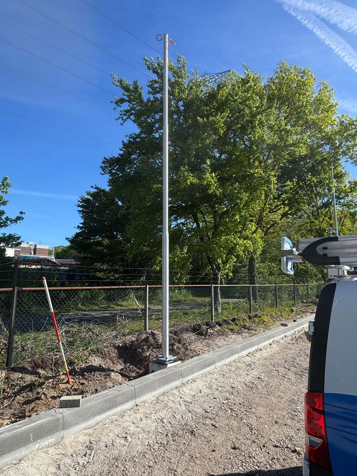Nieuw geplaatste paal langs een pas aangelegde stoeprand, met verse grond waar de kabelsleuf is dichtgemaakt en de servicebus ernaast