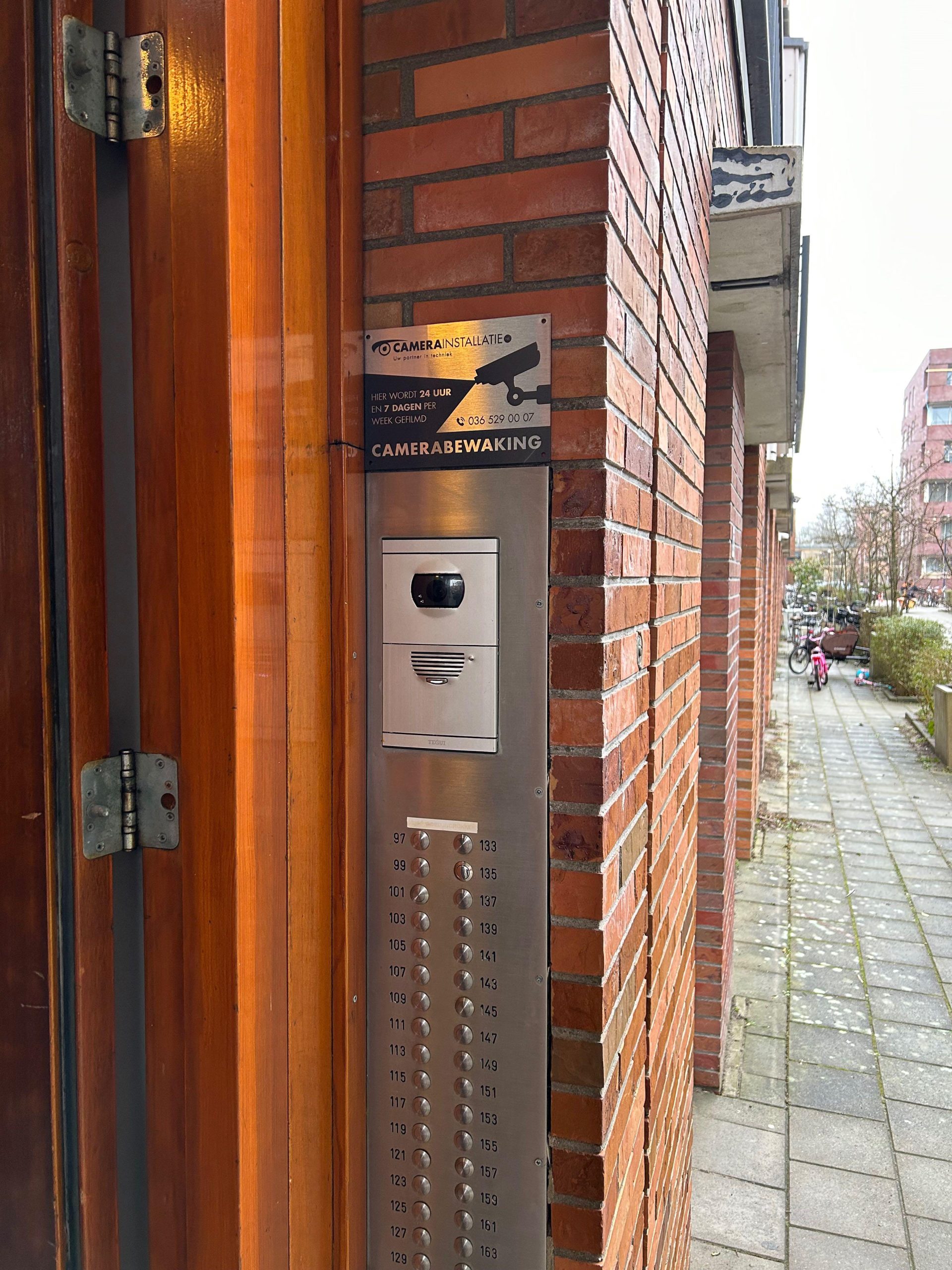 Roestvrijstalen intercompaneel met belknoppen naast de entreedeur van een appartementengebouw