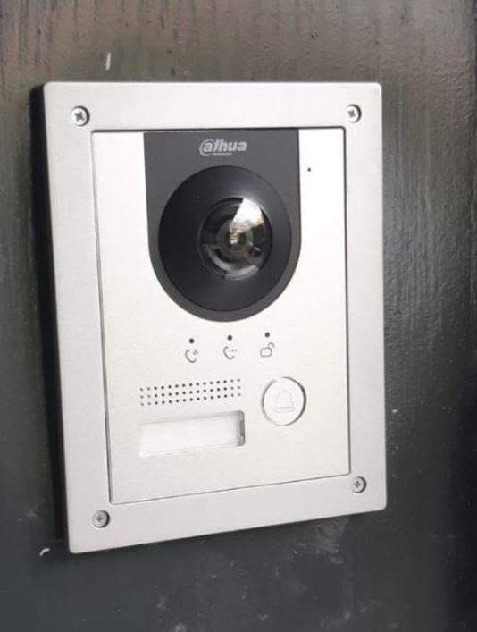 Aluminium video-deurstation met camera, luidspreker, naamplaatje en belknop, strak afgemonteerd op een donkere voordeurpost