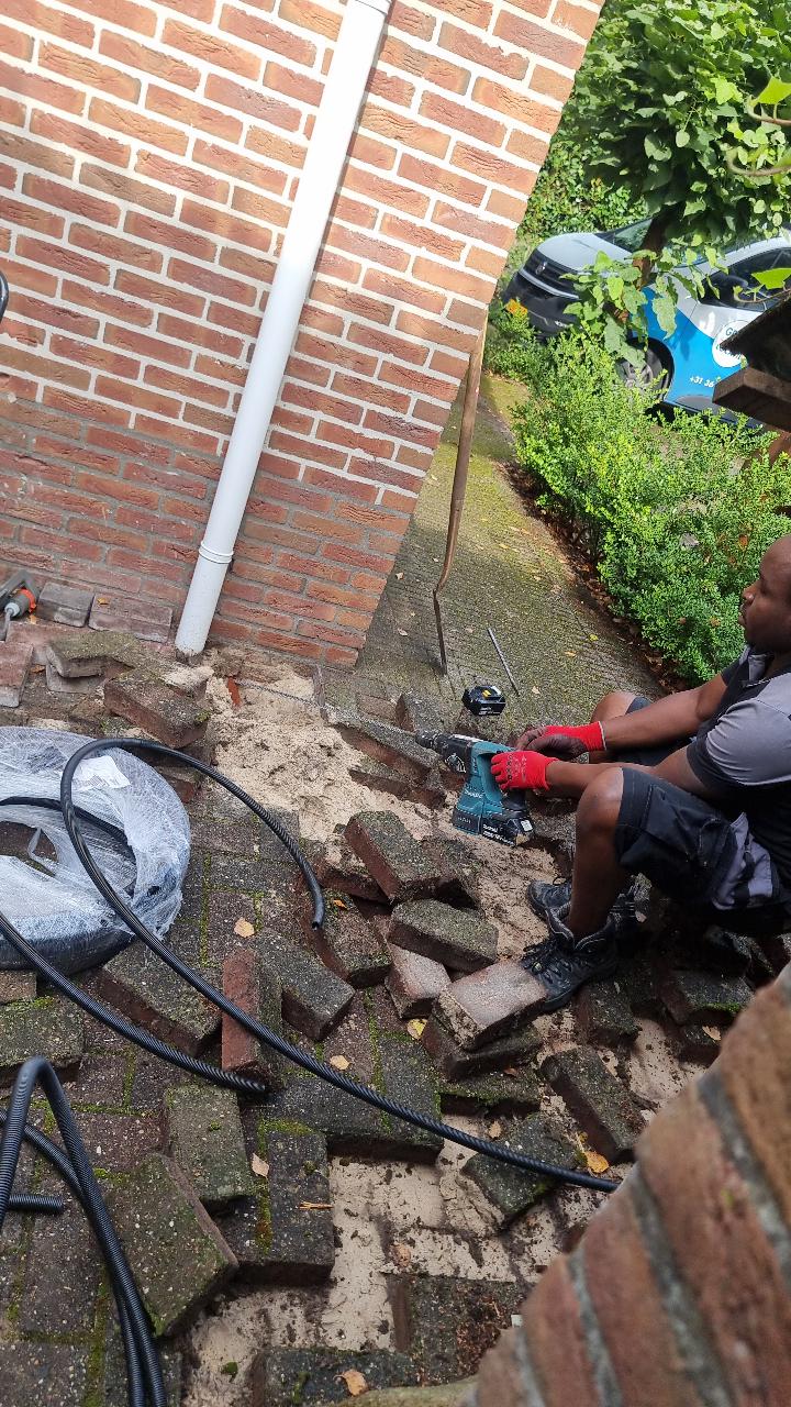 Monteur legt de kabelbuis langs de gevel, onder de opgenomen bestrating door