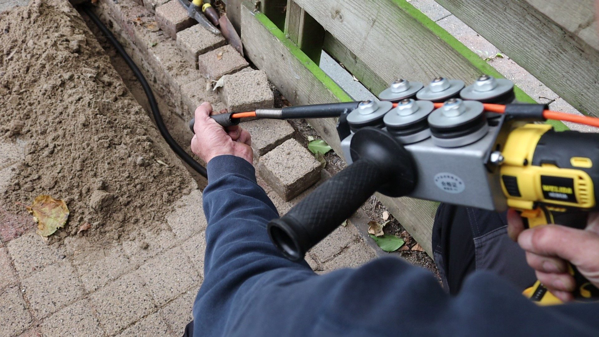 Monteur trekt kabel door een buis langs de tuinschutting