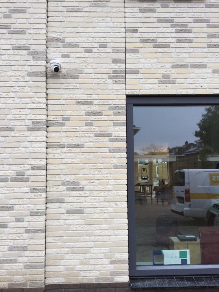Kleine camera op een lichte bakstenen gevel bij de entree