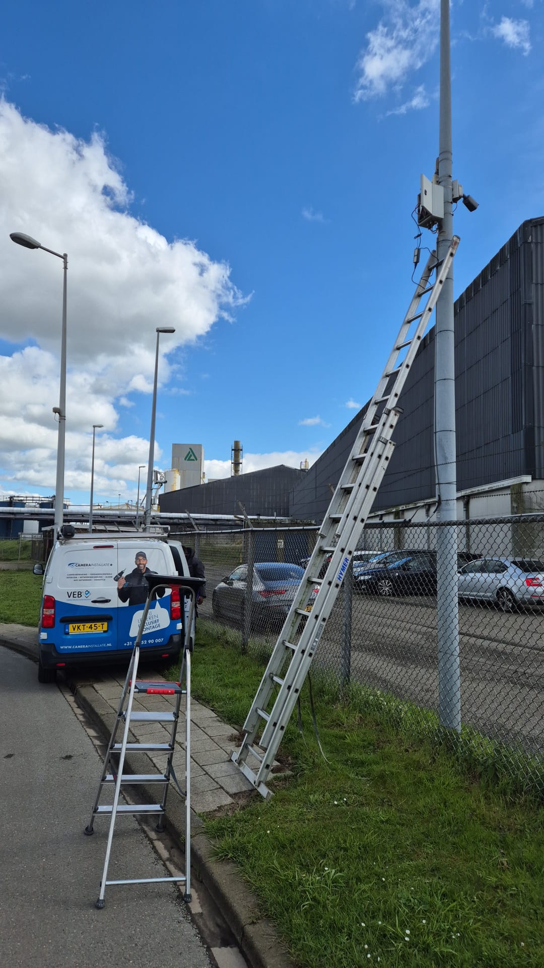 Uitgeschoven ladder tegen een gevel naast de bus, voor een kabelroute op hoogte