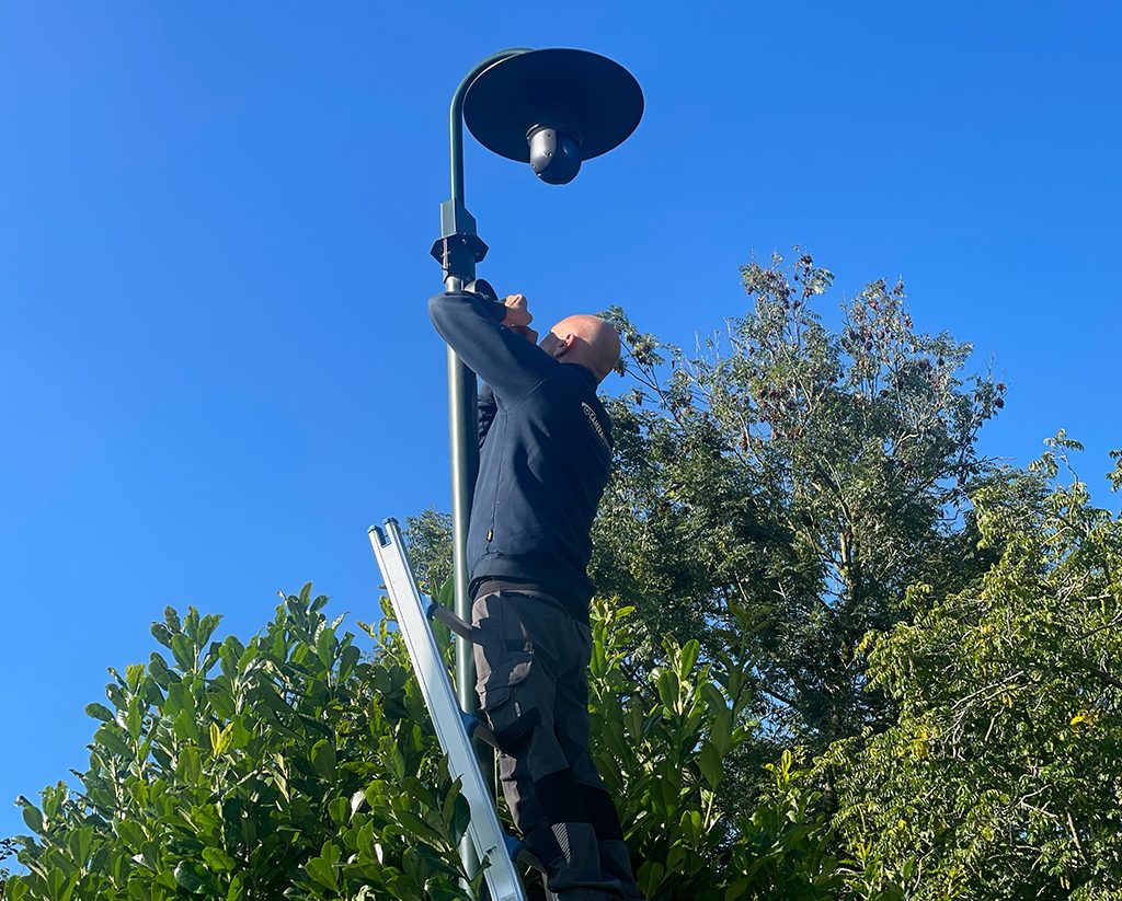Monteur van CameraInstallatie.nl op een ladder monteert een dome-camera onder de kap van een lantaarnpaal