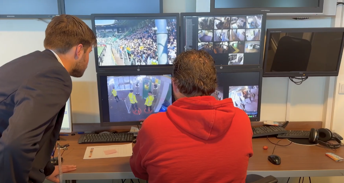 Twee medewerkers kijken mee op de schermenwand in een camerameldkamer