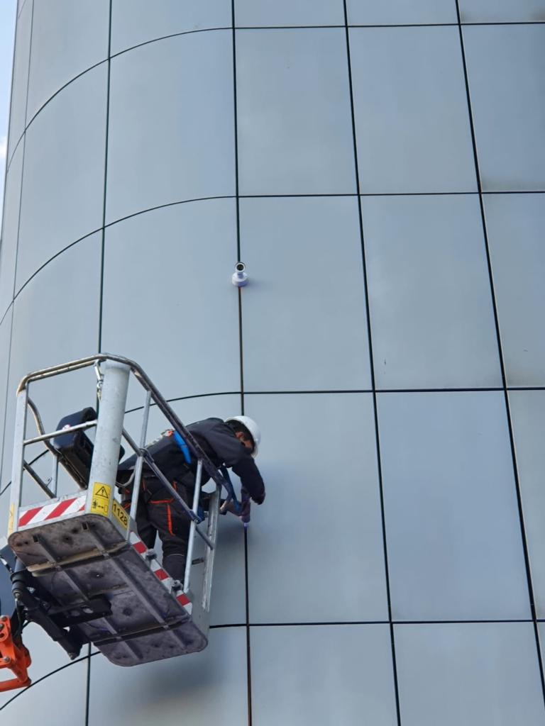 Monteur in een hoogwerker monteert een camera hoog aan een glazen kantoortoren