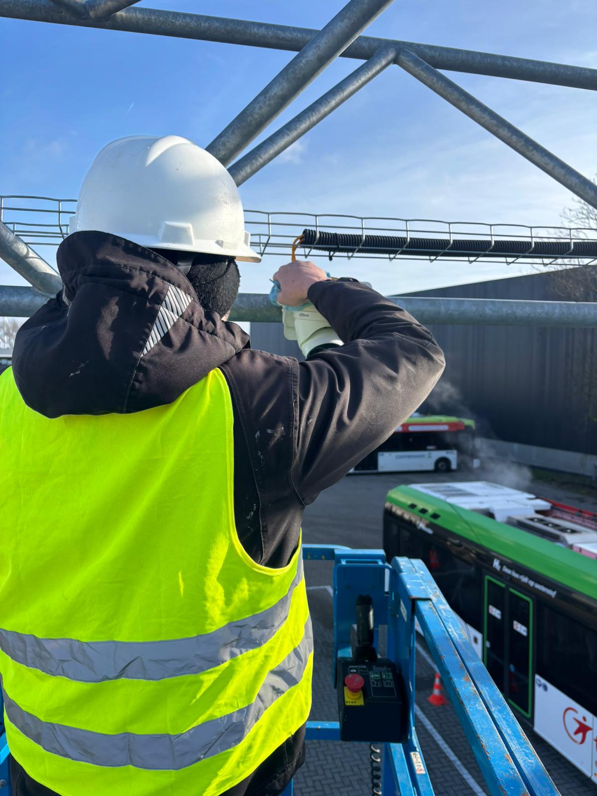 Monteur van CameraInstallatie installeert een beveiligingscamera op een stalen mast op het buitenterrein van een opvanglocatie