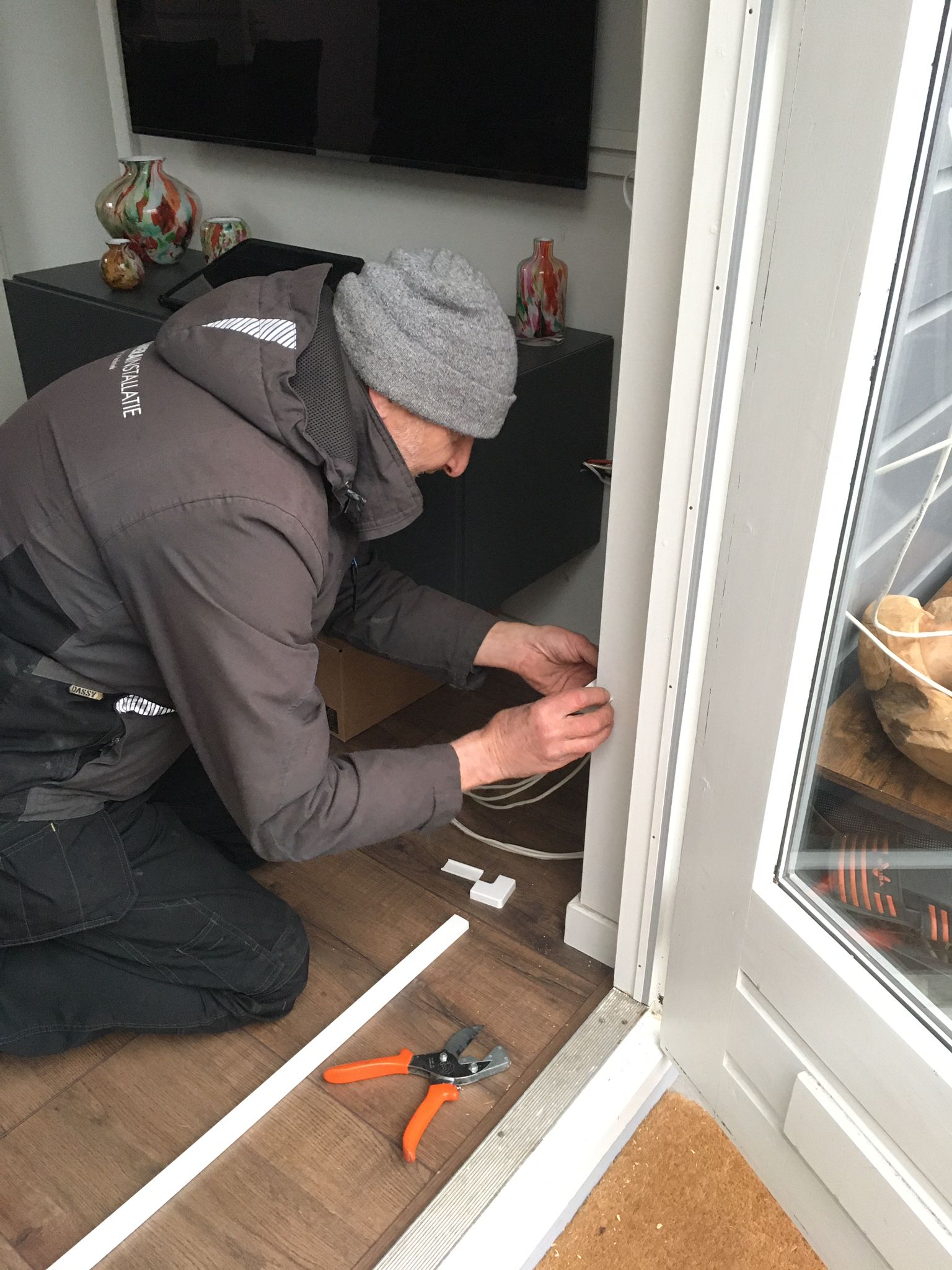 Monteur legt bekabeling weg langs een raamkozijn aan de binnenzijde