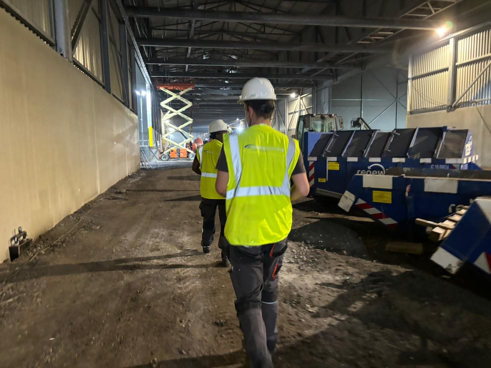 Twee monteurs van CameraInstallatie.nl in veiligheidshesjes lopen met materiaal door een grote bedrijfshal