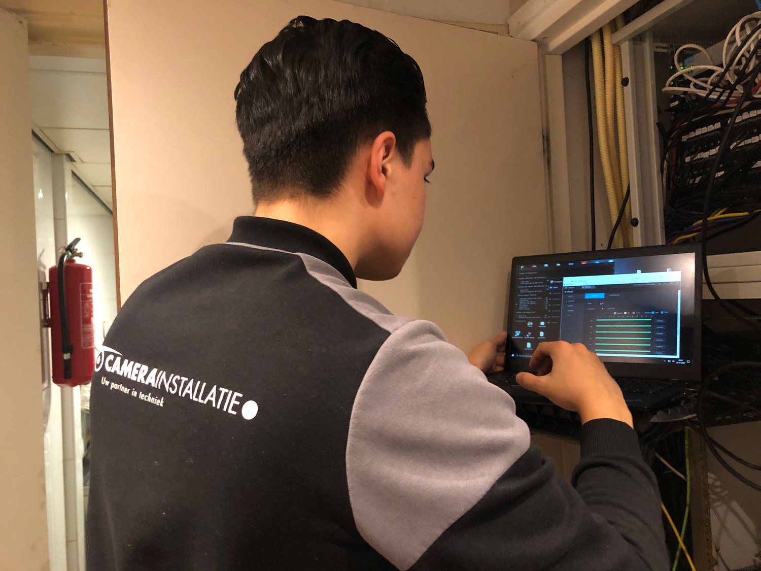 Monteur van CameraInstallatie stelt het camerasysteem in op een laptop bij de patchkast