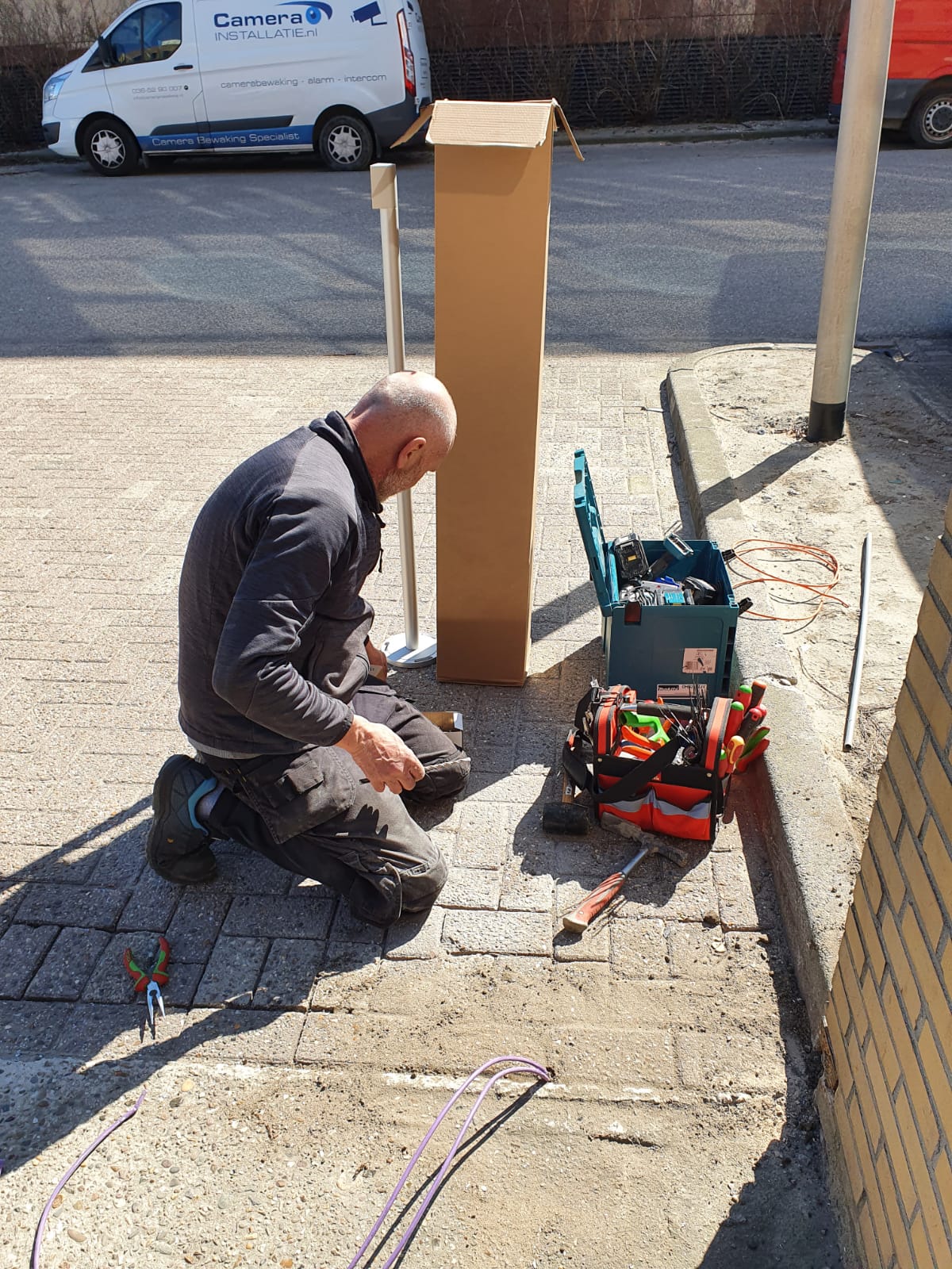Monteur van CameraInstallatie werkt geknield aan de bekabeling bij een buitenpaal op het terrein