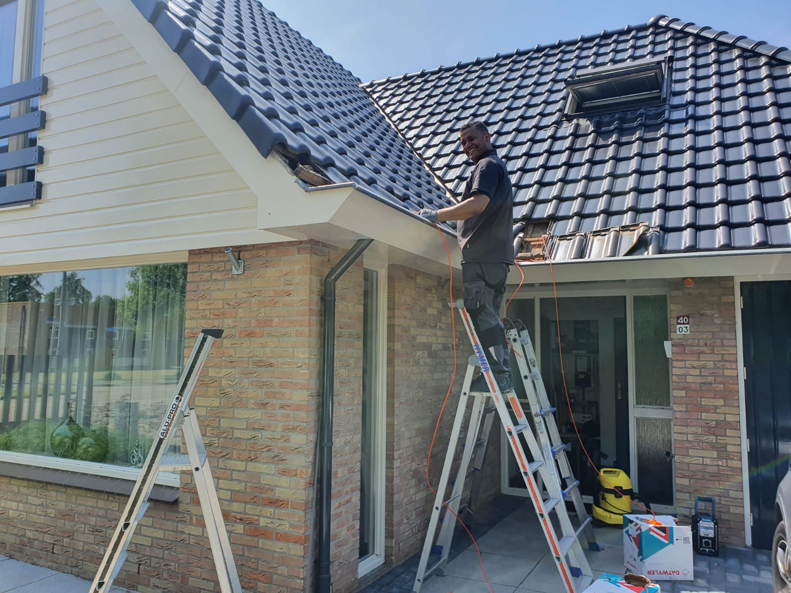 Monteur van CameraInstallatie op een ladder bij de dakrand van een woning