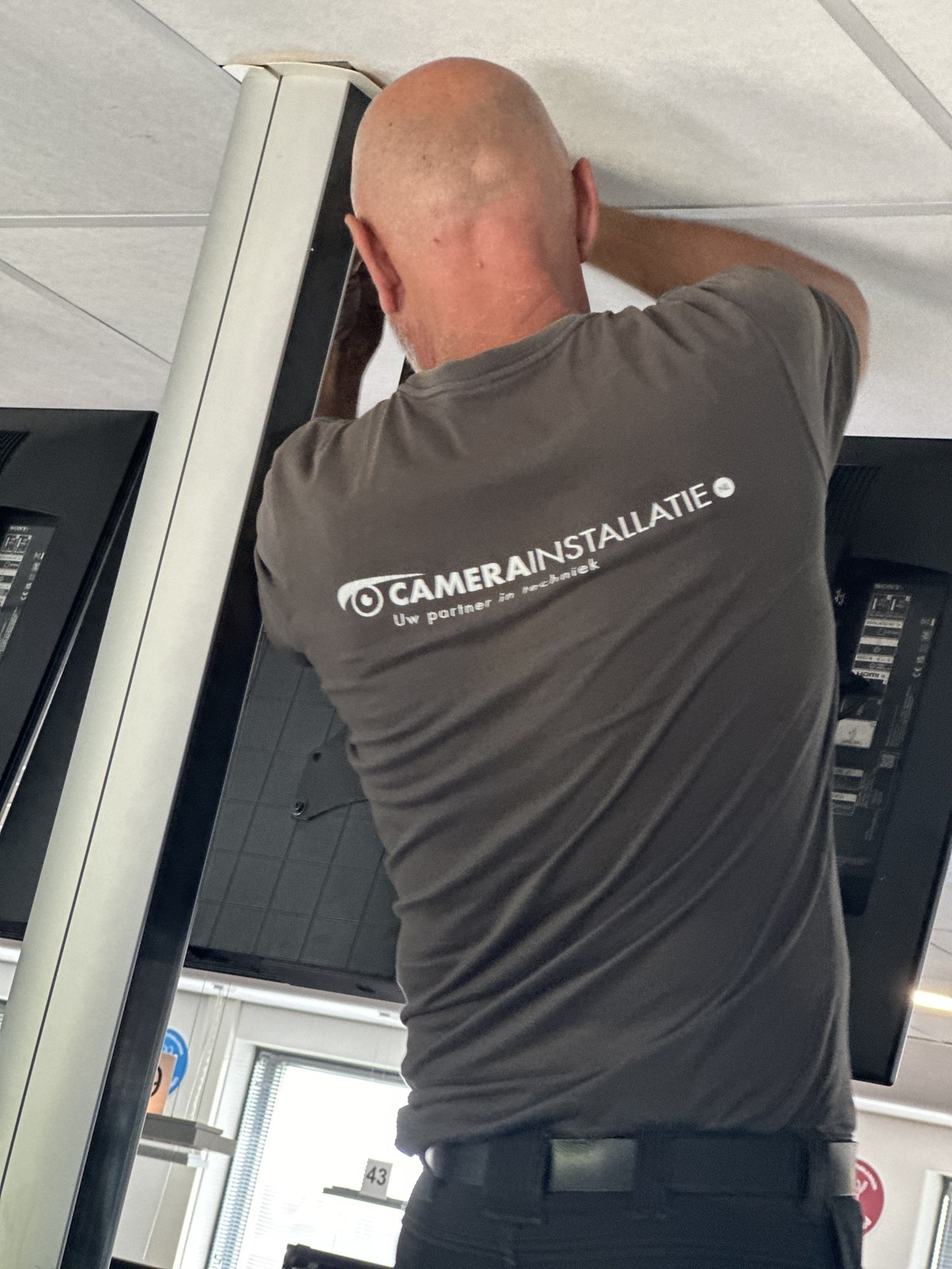 Monteur in bedrijfsshirt werkt aan het plafond tussen de beeldschermen
