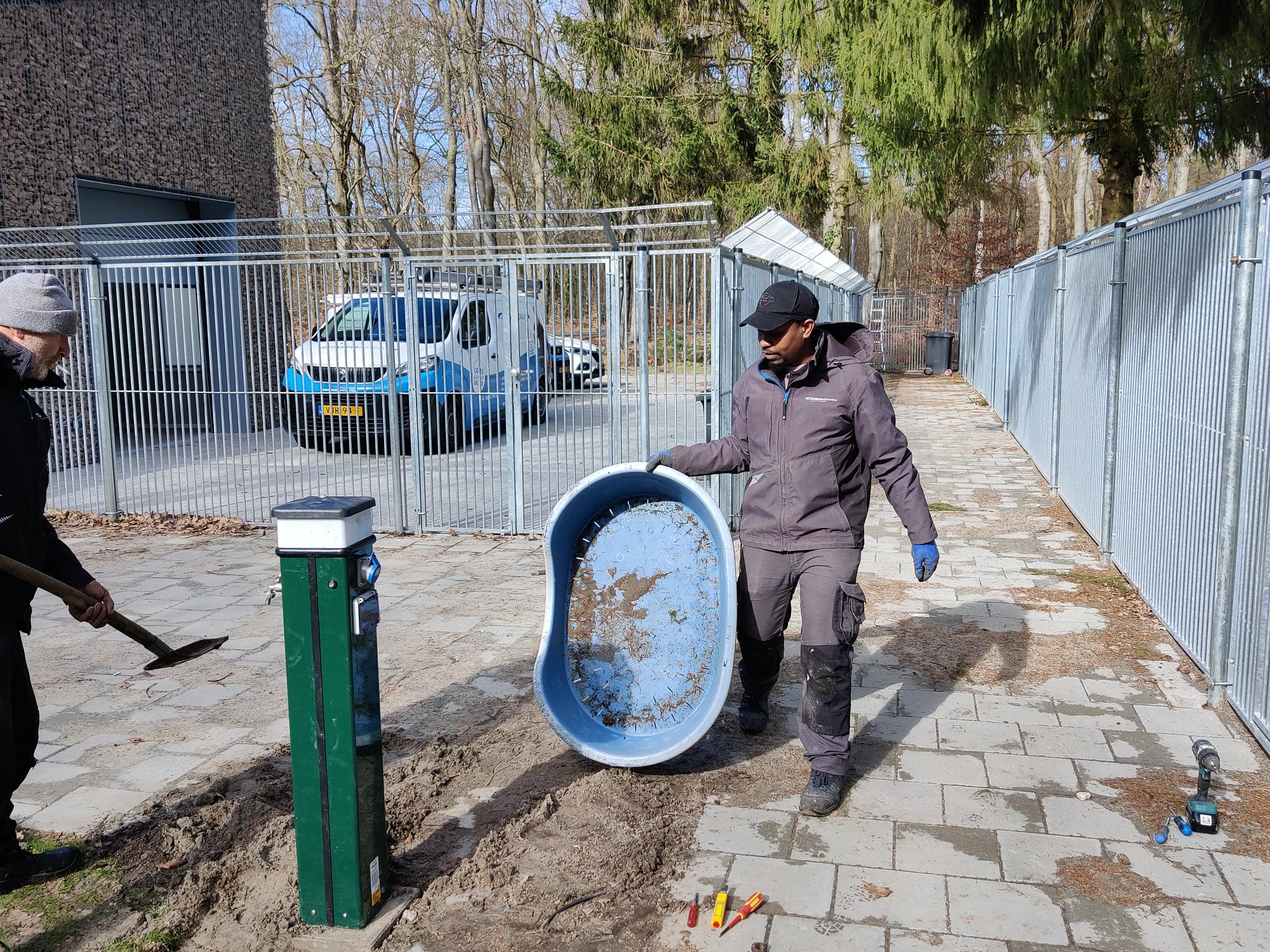 Twee monteurs van CameraInstallatie leggen de grondkabel bij het hek