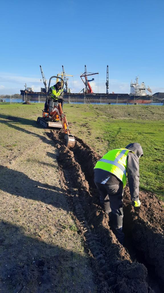 Twee monteurs van CameraInstallatie leggen grondkabel in een sleuf op een buitenterrein