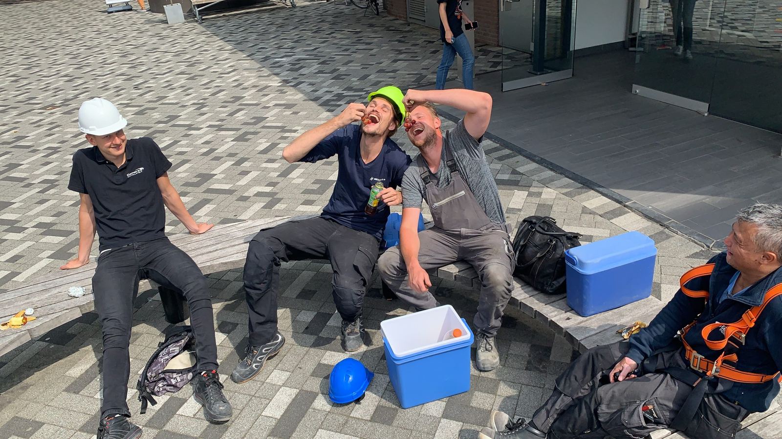 Monteurs van CameraInstallatie nemen samen pauze op locatie, een met veiligheidsharnas en helmen naast de koelbox