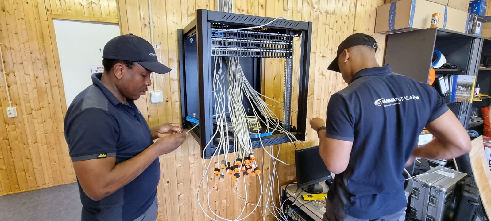 Twee monteurs van CameraInstallatie werken samen aan de technische kast