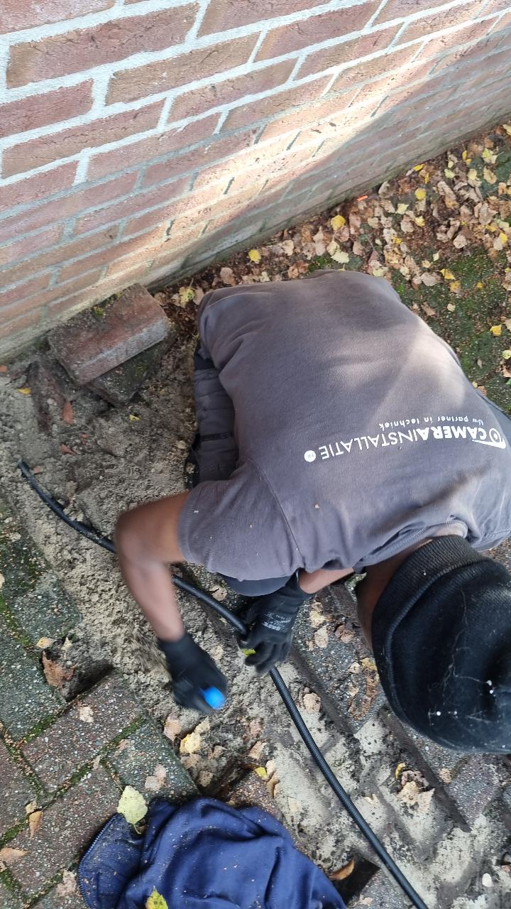 Monteur in bedrijfskleding van CameraInstallatie trekt de netwerkkabel door de buis onder de bestrating