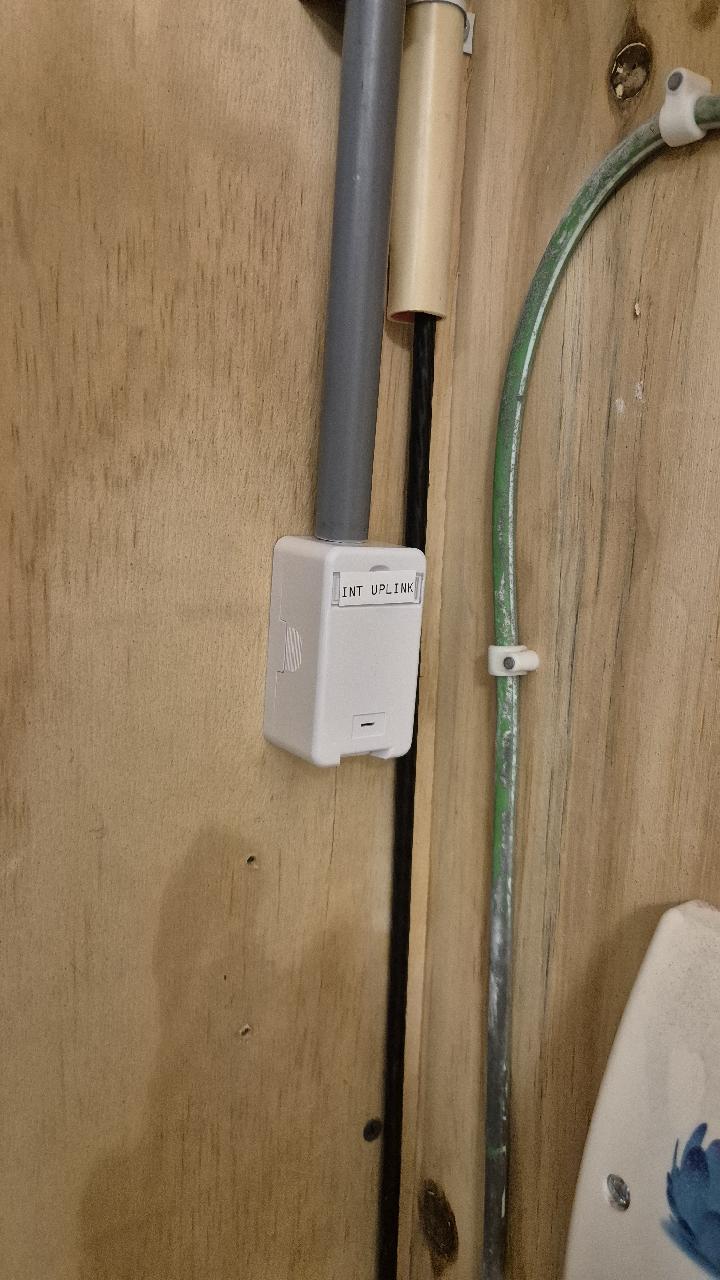 Gelabelde netwerkmodule met de tekst INT UPLINK op een houten wand, met net weggewerkte bekabeling