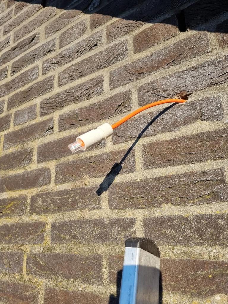Oranje netwerkkabel met stekker komt uit de bakstenen gevel