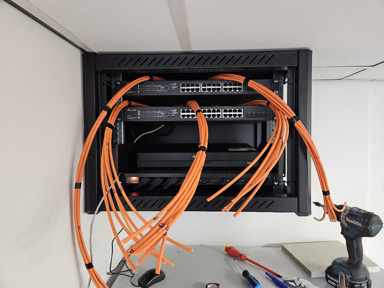 Wandpatchkast met switches en ruime lussen oranje netwerkkabel