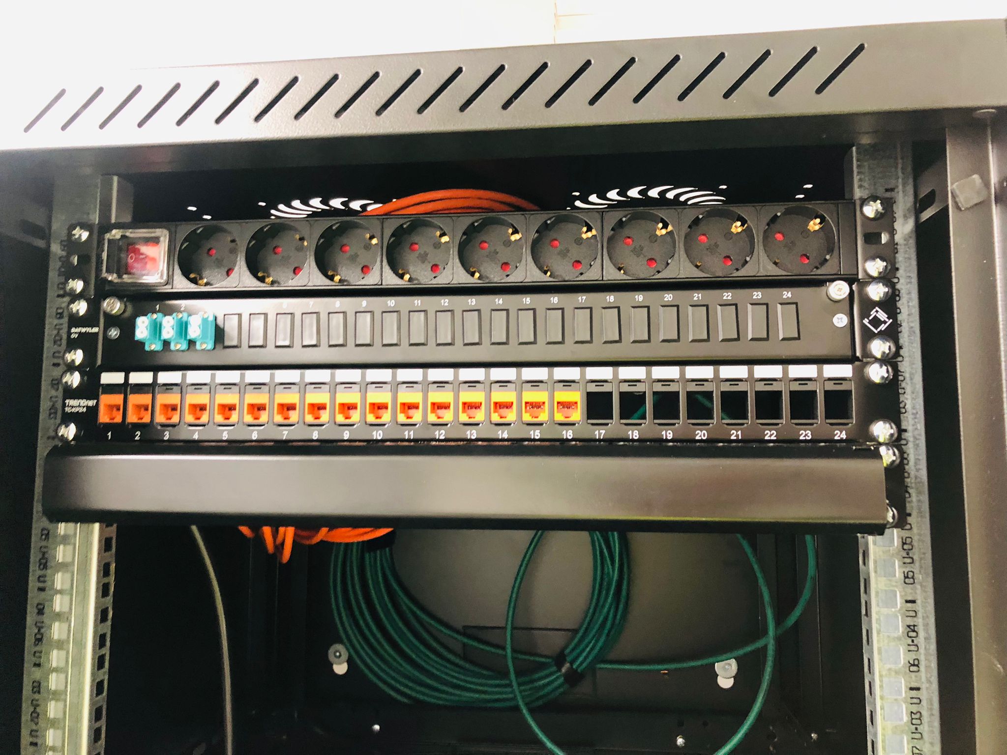 Patchkast met stroomverdeelrail, patchpanelen en opgerolde netwerkkabels