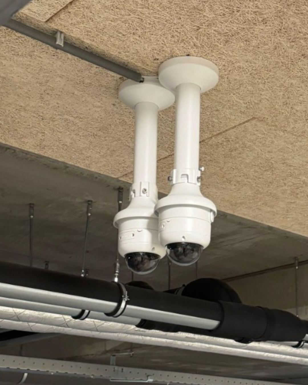 Twee witte camera's van CameraInstallatie op pendelbeugels aan een plafond, netjes weggewerkt langs de leidingen