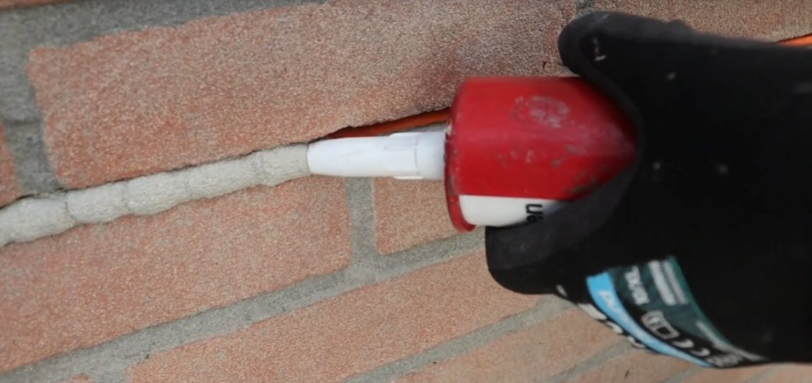 Monteur spuit de voeg weer dicht met kit nadat de camerakabel is weggewerkt in de gevel