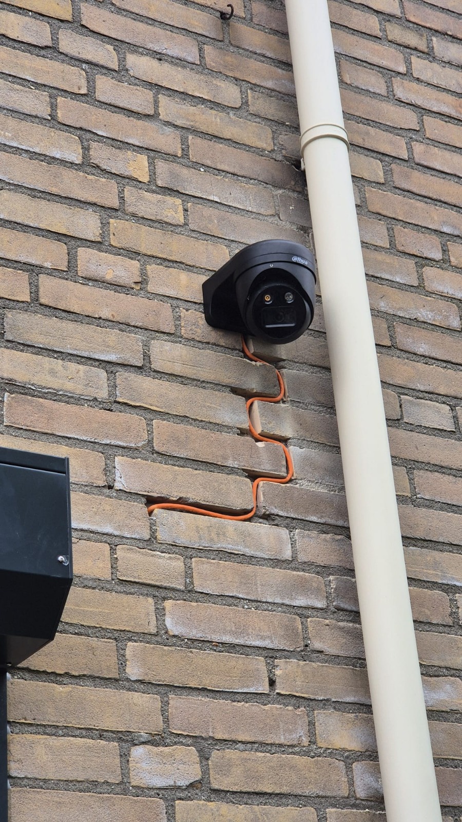 Netwerkkabel weggewerkt in de uitgeslepen voeg van een bakstenen gevel, van de camera naar beneden